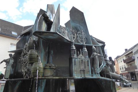 Une fontaine artistique avec différentes sculptures, qui représente des figures dynamiques. La surface en bronze reflète la lumière et crée un jeu intéressant d'ombres et de formes.