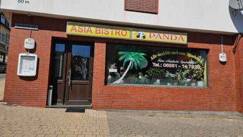 Ein asiatisches Bistro mit dem Namen "Panda". Die Fenster sind mit einem Palmenmotiv dekoriert und es gibt eine Telefonnummer für Bestellungen.