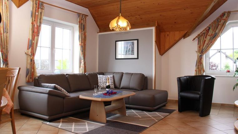 Ein gemütliches Wohnzimmer mit einer modernen Couch und einem runden Tisch. Helle Fenster und eine Holzdecke sorgen für eine einladende Atmosphäre.