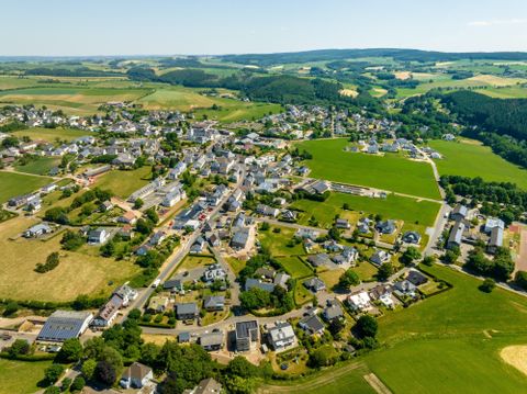 Eine malerische Luftaufnahme eines kleinen Dorfes umgeben von grünen Feldern und Hügeln. Die Häuser sind harmonisch in die Landschaft integriert.
