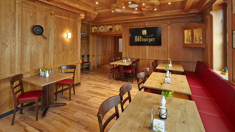 Ein gemütliches Restaurant mit Holzwänden und rustikalen Tischen. Rote Sitze und kleine Pflanzen sorgen für eine einladende Atmosphäre.
