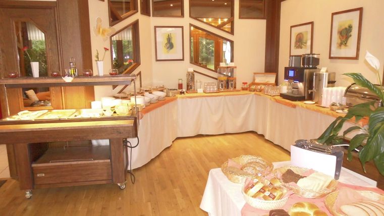 Ein eleganter Frühstücksraum mit einem Buffet voller frischer Backwaren und Getränken. Die warme Holzverkleidung und die dekorativen Bilder verleihen dem Raum eine einladende Atmosphäre.