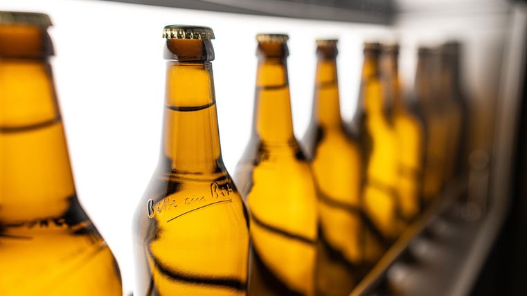 Een reeks bruine bierflessen staat op een rij. De flessen reflecteren het licht en creëren een aantrekkelijk effect.