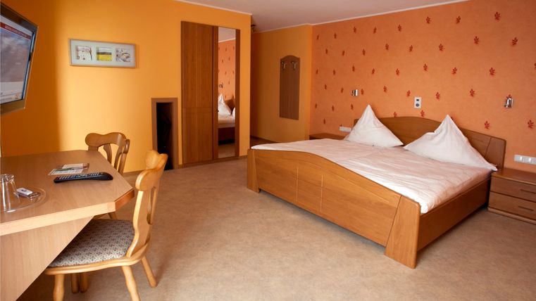 Ein gemütliches Hotelzimmer mit einem großen Bett und einem Schreibtisch. Die Wände sind in einem warmen Orange gehalten, und es gibt einen Fernseher.