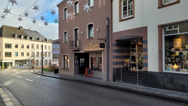 Eine ruhige Straße mit Geschäften und einem Café. Über der Straße hängen dekorative Sterne.