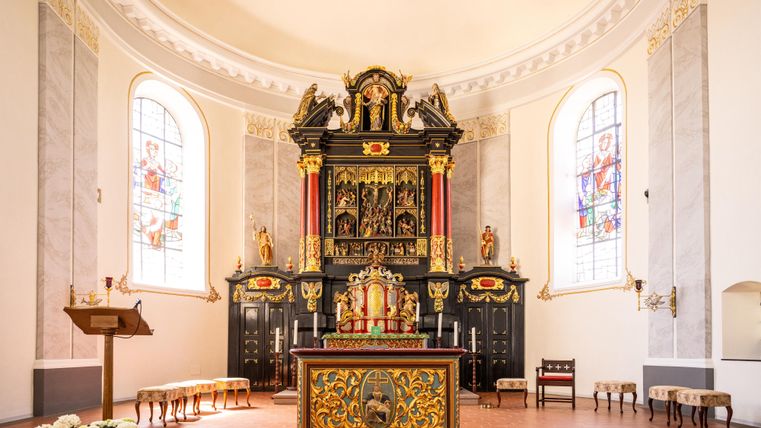 A beautiful church space with an artistically designed altar in the background. Colorful windows let in gentle light.