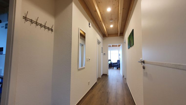Ein heller Flur mit Holzdecke und modernen Wänden. Am Ende des Flurs ist ein Wohnzimmer sichtbar.