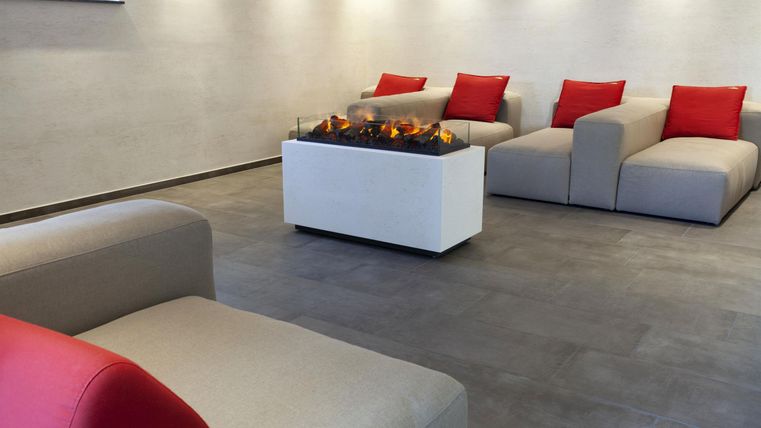 Ein modernes Wohnzimmer mit gemütlichen Sofas und roten Kissen. In der Mitte befindet sich ein eleganter Tisch mit einem Kamin.