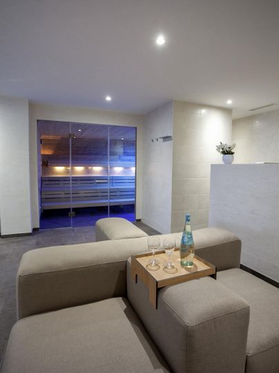 Ein modernes Wohnzimmer mit einem bequemen Sofa und einem kleinen Tisch. Durch die Fenster ist ein sanftes Licht zu sehen.