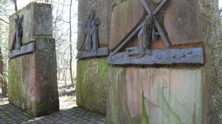 Ein Denkmal mit zwei großen Steinsäulen, die Reliefs von Figuren darstellen. Umgeben von Bäumen in einer ruhigen, natürlichen Umgebung.