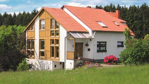 Ein schönes Haus mit rotem Dach und großen Fenstern. Es liegt umgeben von grünem Gras und Bäumen.