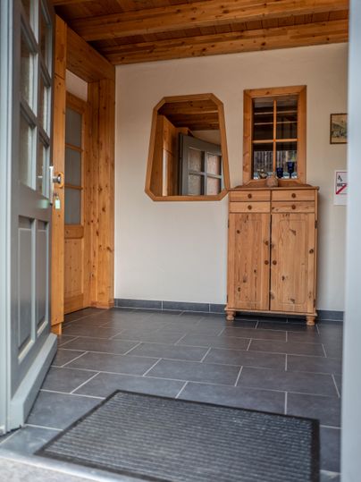 Ein heller Eingangsbereich mit Holzdetails und einem großen Spiegel. Auf dem Boden liegt ein dunkler Teppich und ein Holzschrank steht an der Wand.