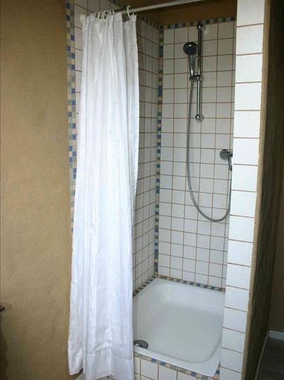 Eine einfache Duschkabine mit einer weißen Duschvorhang und Fliesenwänden. Der Duschkopf ist an der Wand angebracht.