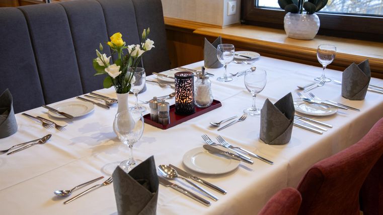 Ein elegant gedeckter Tisch mit Besteck, Gläsern und Blumen. Die Einrichtung ist modern und einladend.