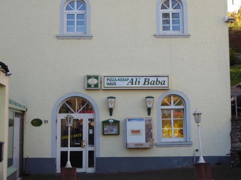 Ein Restaurant mit der Bezeichnung "Ali Baba" ist an einer hellen Gebäude-Fassade zu sehen. Die Fenster sind oval und die Eingangstür lädt zum Betreten ein.