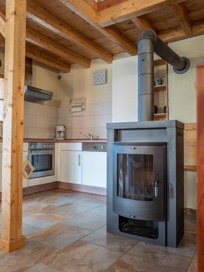 Eine moderne Küche mit einem Holzofen und einem offenen Raumkonzept. Die Holzbalken verleihen der Umgebung eine gemütliche Atmosphäre.