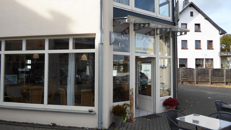 Ein schönes Café an einer ruhigen Straße mit großen Fenstern. Draußen stehen Tische und Stühle für Gäste.