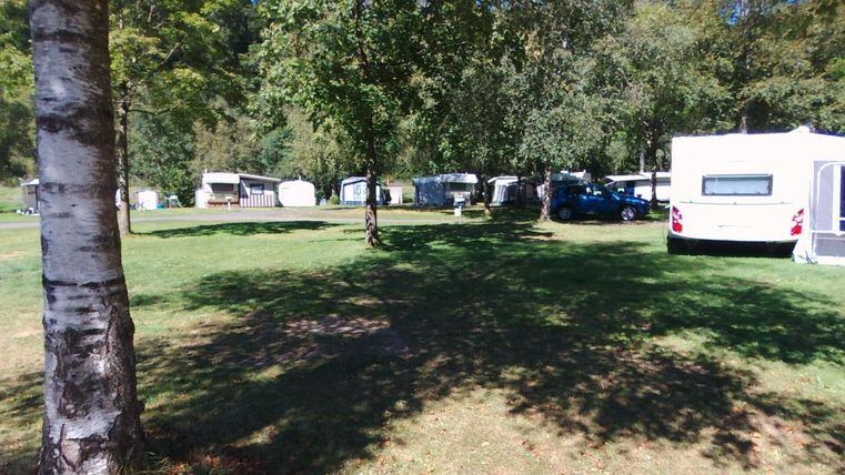Ein Campingplatz mit mehreren Wohnwägen und grünen Rasenflächen. Bäume spenden Schatten in einer ruhigen Umgebung.