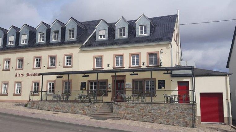 Ein charmantes Hotel mit zwei Etagen und einem hohen Dach. Die Fassade ist hell und einladend, mit Sitzgelegenheiten im Freien.