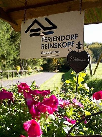Ein Willkommensschild des Feriendorfs Reinskorp mit bunten Blumen im Vordergrund. Der Weg zum Empfang ist klar und einladend.