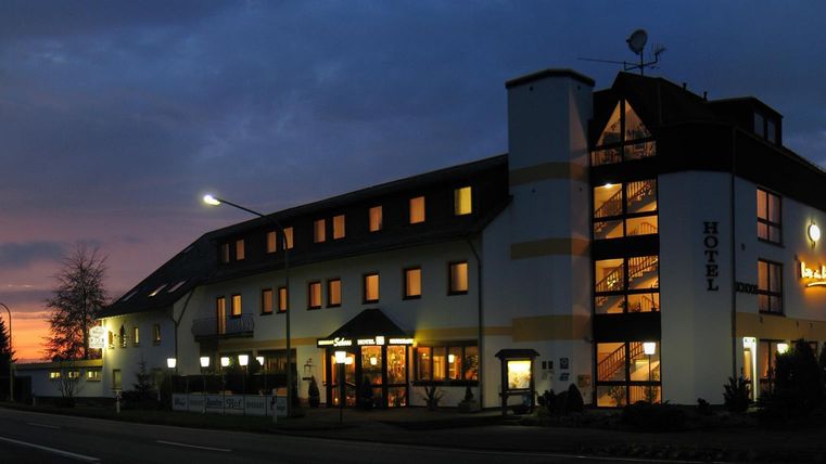 Ein Gebäude eines Hotels bei Sonnenuntergang. Die Lichter sind hell und die Umgebung wirkt einladend.