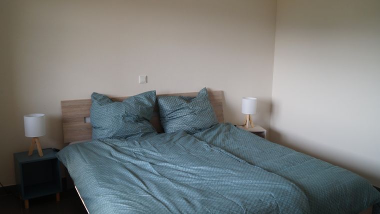 Ein gemütliches Schlafzimmer mit einem großen Bett und blauen Bettdecken. Neben dem Bett stehen zwei Nachttische mit Lampen.