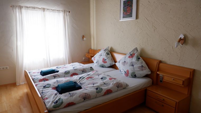 Ein gemütliches Schlafzimmer mit zwei Betten und farbenfrohen Kissen. Die Fenster lassen viel Licht herein und schaffen eine einladende Atmosphäre.