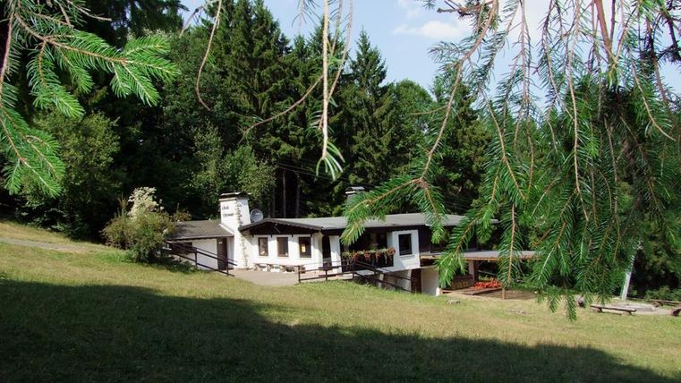 Une maison calme dans un environnement verdoyant avec des arbres en arrière-plan. L'atmosphère ensoleillée transmet un sentiment de détente et de connexion avec la nature.