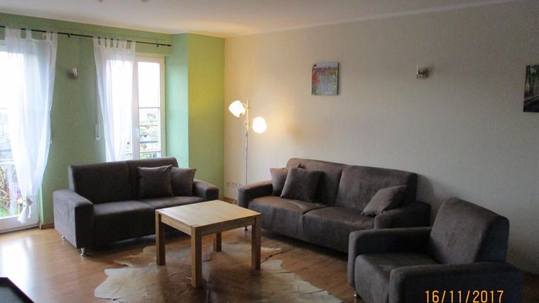 Ein modernes Wohnzimmer mit grauen Sofas und einem Holztisch. Die Wände sind hellgrün, und große Fenster sorgen für viel Licht.