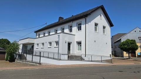 A modern, white building on a street corner. It has large windows and a ramp that makes it easier to enter.
