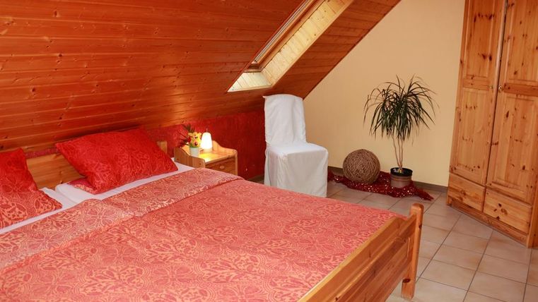 Ein gemütliches Schlafzimmer mit einem Holzdecke und roten Kissen. Im Raum stehen eine Pflanze und ein Kleiderschrank.