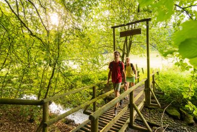 Two hikers cross a wooden bridge in the forest.