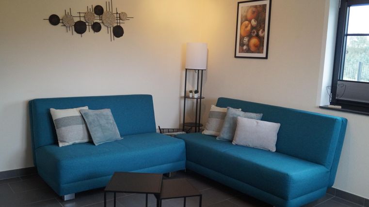 Ein modernes Wohnzimmer mit zwei türkisfarbenen Sofas und einer schwarzen Beistelltisch. An der Wand hängen ein Kunstwerk und ein Bild von Früchten.