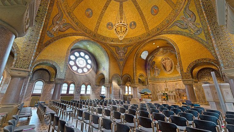 Magnificent interior view of the Church of the Redeemer in Gerolstein with golden mosaics, angel representations, and a large chandelier under a dome.