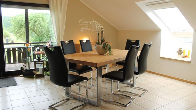 Ein modernes Esszimmer mit einem Holztisch und sechs schwarzen Stühlen. Große Fenster sorgen für viel Licht und einen Blick ins Grüne.