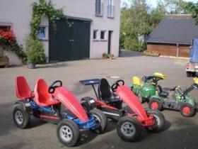 Ein Hof mit mehreren Kettcars in verschiedenen Farben. Im Hintergrund sind Gebäude und Pflanzen zu sehen.