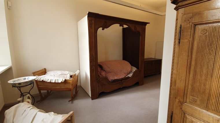 Ein einfaches, helles Zimmer mit einem Holzschrank und einem großen Bett. Neben dem Bett steht ein kleiner Tisch und ein Stuhl.