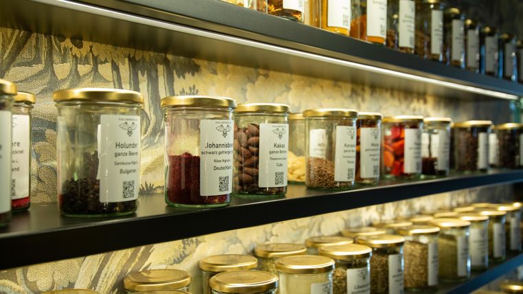 Eine gut sortierte Wand mit Gläsern voller Gewürze und Kräuter. Die Gläser haben etikettierte Beschriftungen und sind in einer ansprechenden Anordnung präsentiert.