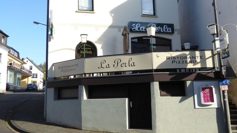 Een restaurant met de naam "La Perla" op een hoek van de straat. De gevel toont een moderne inrichting met een uitnodigende buitenruimte.