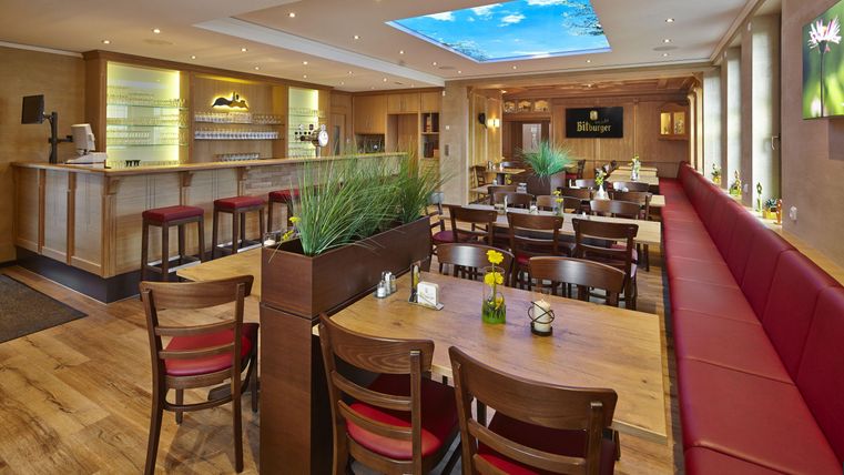 Ein modernes Restaurant mit holzernen Tischen und roten Bänken. Deckenlichter schaffen eine angenehme Atmosphäre.