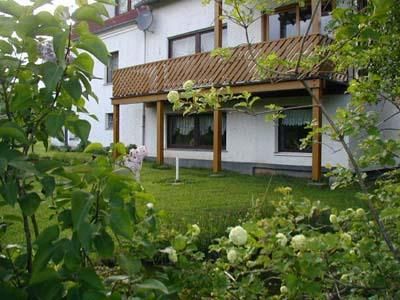 Ein gemütliches Haus mit einem Holzveranda und grünen Pflanzen im Vordergrund. Der Garten ist gepflegt und lädt zum Entspannen ein.