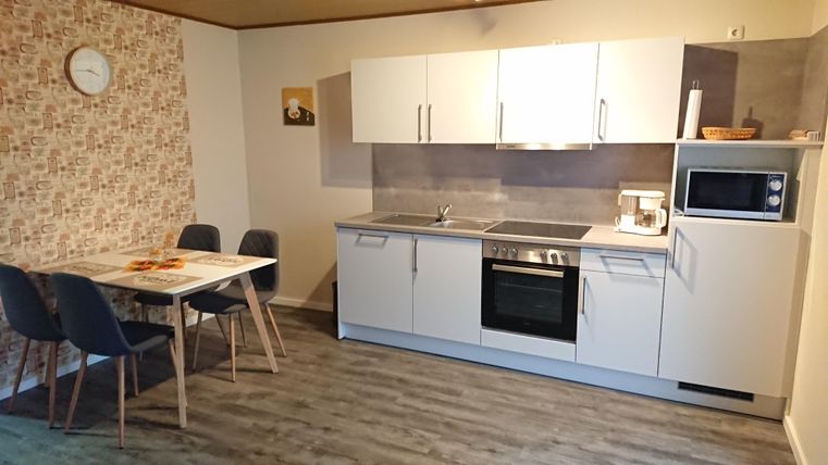 Eine moderne Küche mit weißen Schränken und einem Esstisch. Sie ist gut ausgestattet und hat einen freundlichen, einladenden Look.