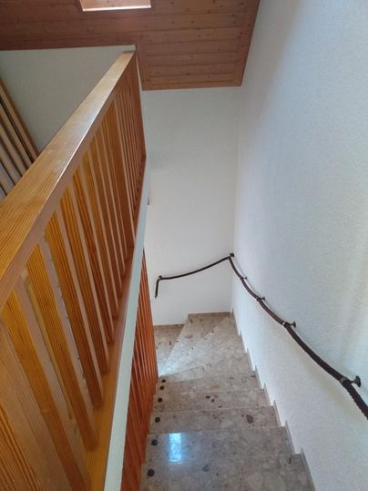 Eine Treppe mit Steinboden und einem Holzgitter. An der Wand verläuft ein Handlauf.