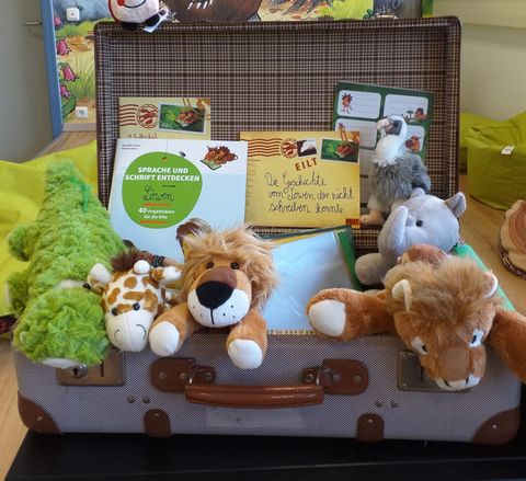 Ein Koffer voller Plüschtiere, darunter ein Löwe, eine Giraffe und ein Krokodil. Zudem sind einige Karten und eine Notiz im Koffer sichtbar.