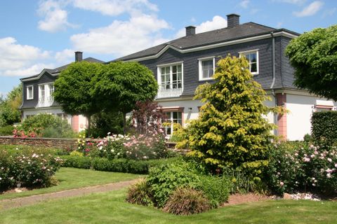 Ein schönes Haus mit einem gepflegten Garten. Rund um das Haus wachsen große Bäume und bunte Blumen.
