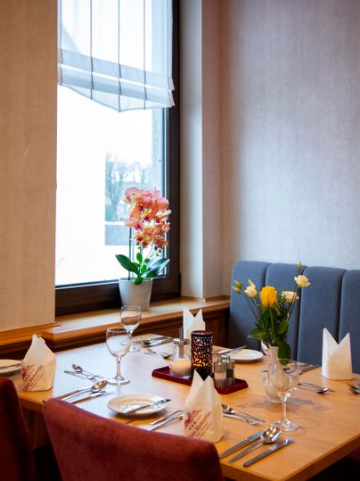 Ein gemütlicher Tisch in einem Restaurant, schön gedeckt mit Gläsern und Besteck. Auf dem Tisch stehen Blumen in einer Vase und eine ansprechend dekorierte Atmosphäre.