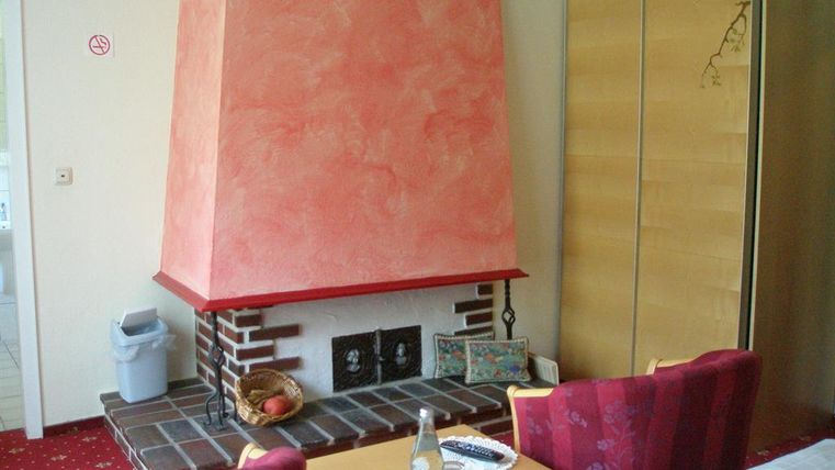 Ein Wohnzimmer mit einem roten Kamin und gemütlichen Sitzgelegenheiten. Der Raum hat einen roten Teppich und einige Möbelstücke in Holzoptik.