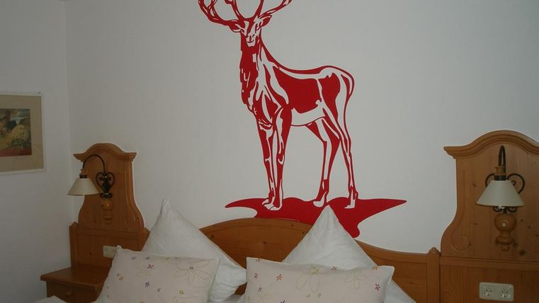 Ein gemütliches Zimmer mit zwei Betten und roten Kissen. An der Wand ist ein rotes Wanddesign eines majestätischen Rothirschs.