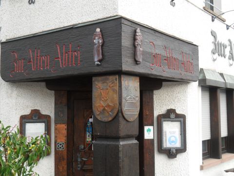 Ein traditionelles Gasthaus mit dem Namen "Zur Alten Adlerei". Der Eingangsbereich zeigt kunstvolle Holzschnitzereien und alte Wappen.