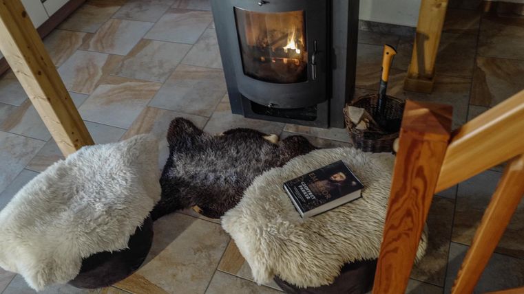 Ein gemütlicher Raum mit einem Holzofen und zwei Sitzen, die mit Fellen bedeckt sind. Ein Buch liegt auf einem der Sitze.